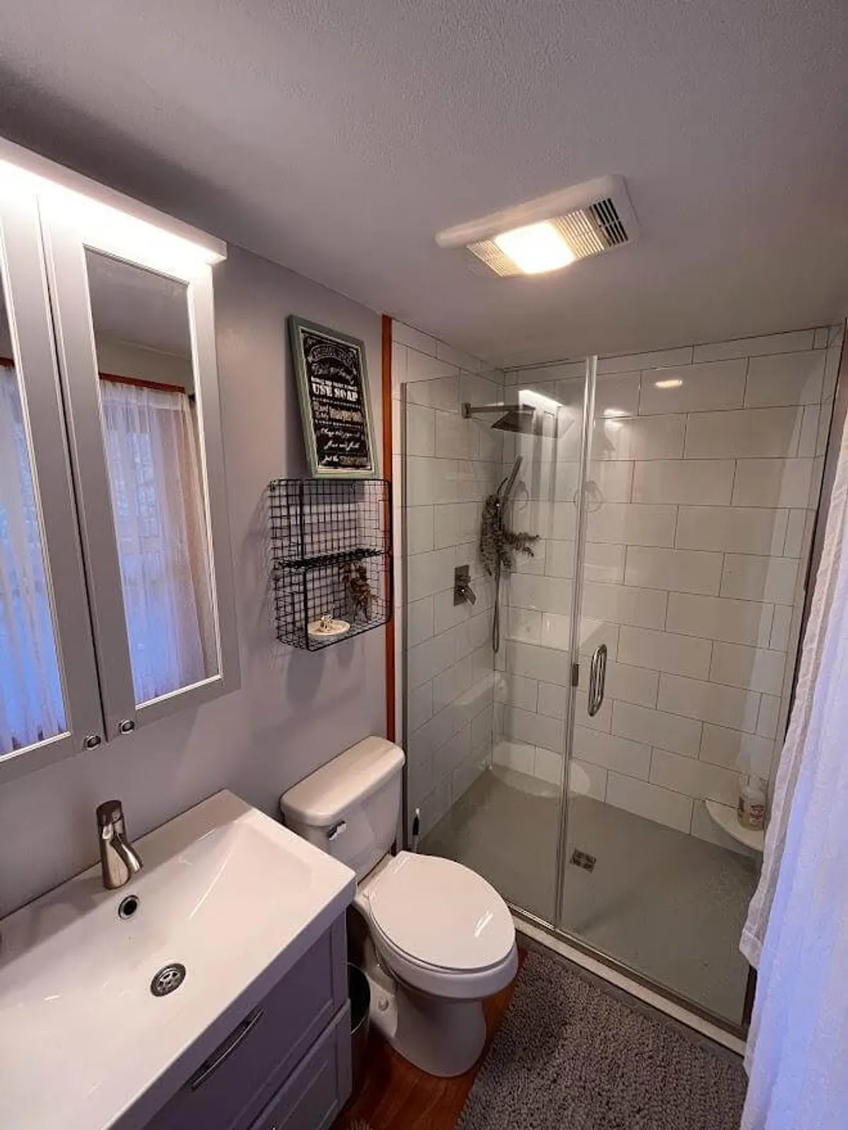 A well-appointed bathroom featuring a vanity sink, shower enclosure, decorative wall art, and a toilet. The fresh, welcoming design and modern fixtures suggest comfort and easy access for all guests.