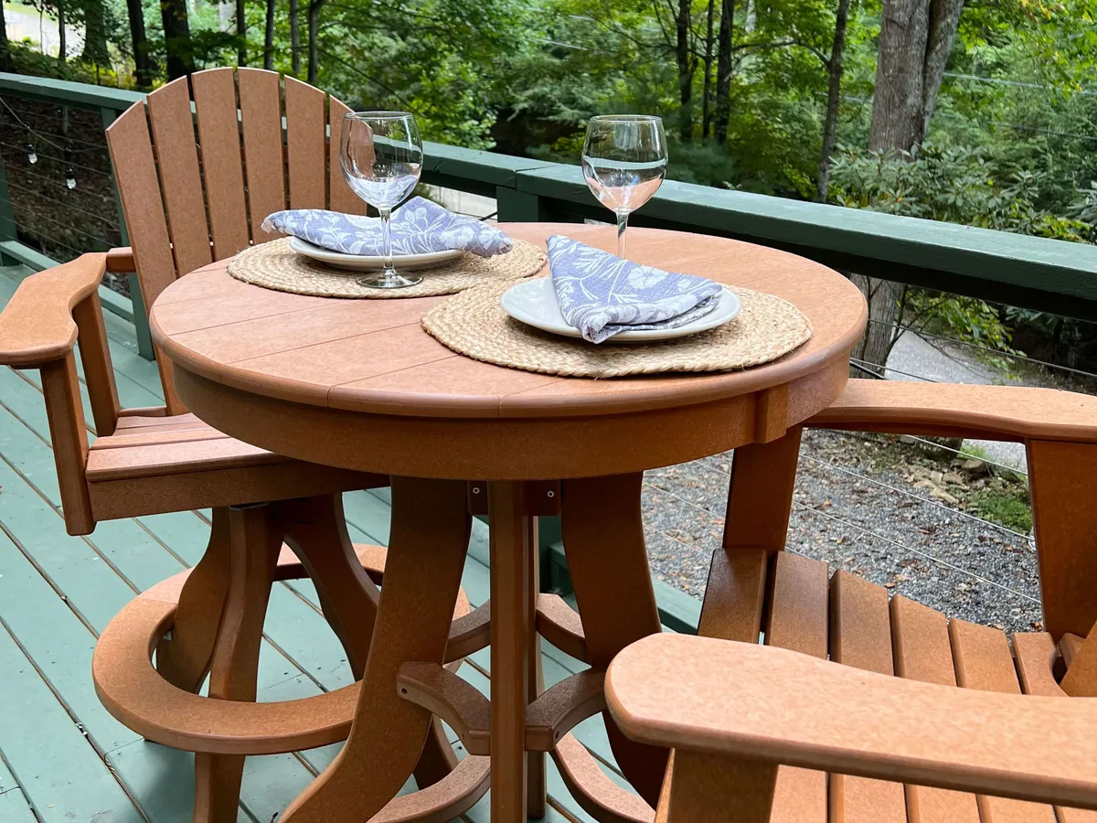 An exterior dining area with a round table and wooden chairs, thoughtfully set with wine glasses and napkins, overlooking a natural landscape. The atmosphere is open, intimate, and perfectly suited for romantic outdoor dining during sunset.