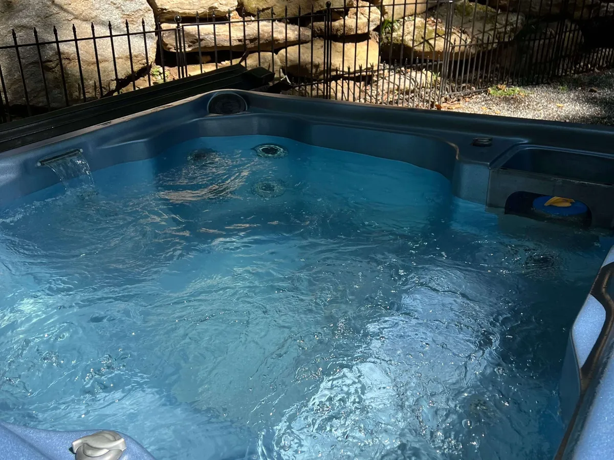 An inviting hot tub set among rocks and a rustic fence, seamlessly blending into the mountain landscape. The space is open to the sky, suggesting tranquil sunset views and the possibility of stargazing, surrounded by nature for privacy.