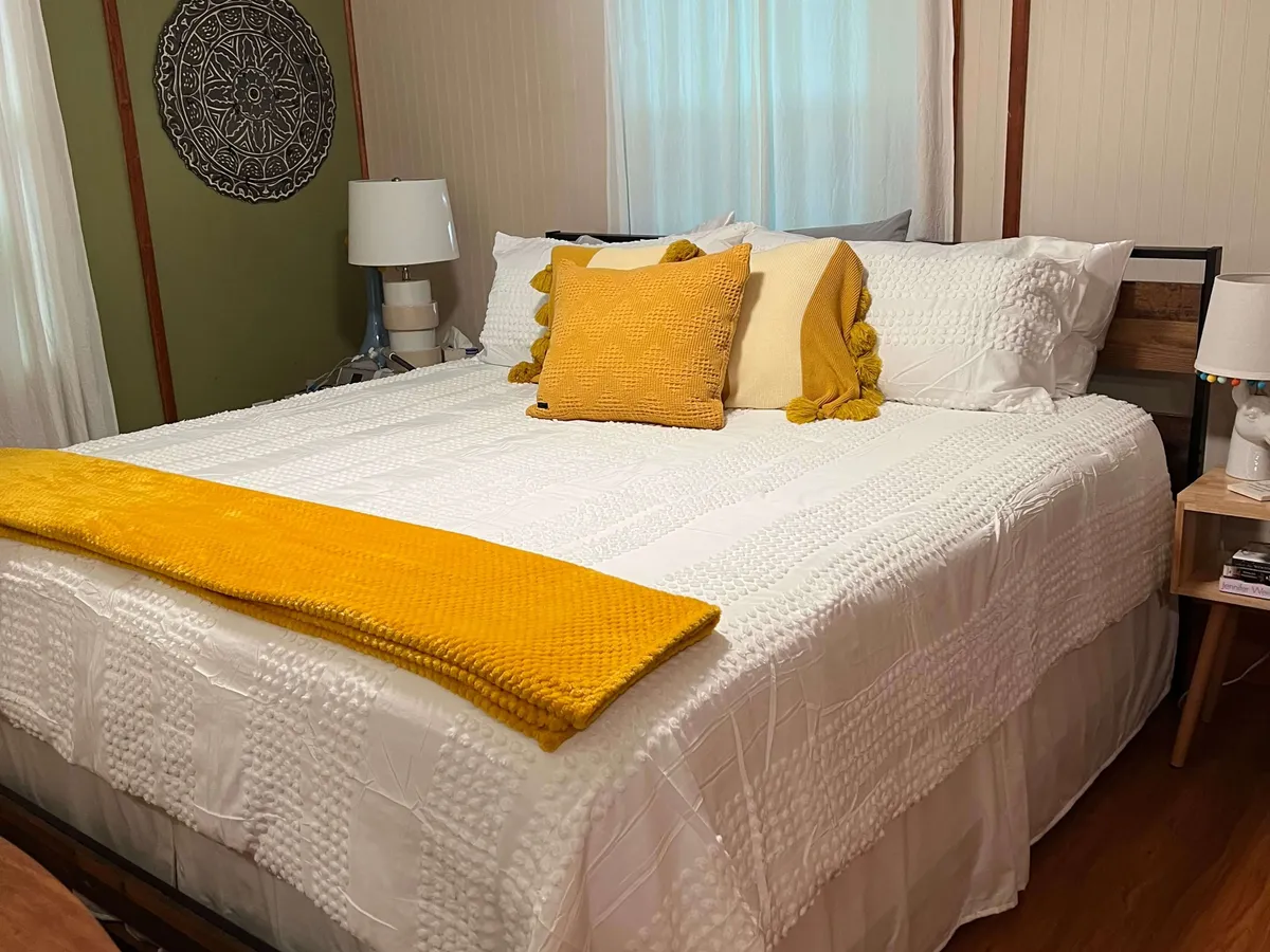 A warmly lit bedroom with a bed adorned with a yellow throw blanket and pillows, flanked by bedside tables with lamps and decorative wall art. The overall mood is welcoming and comfortable, ideal for unwinding after a day outdoors.