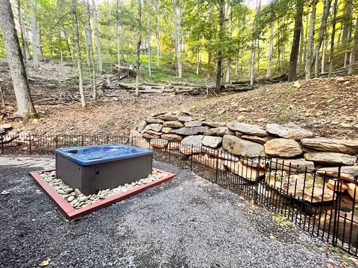 A private outdoor hot tub surrounded by a stone wall and nestled at the edge of a forest. The setting is tranquil, with the hot tub steaming against the cool air and a dense woodland providing privacy. The space feels inviting for relaxing after a day on the slopes.