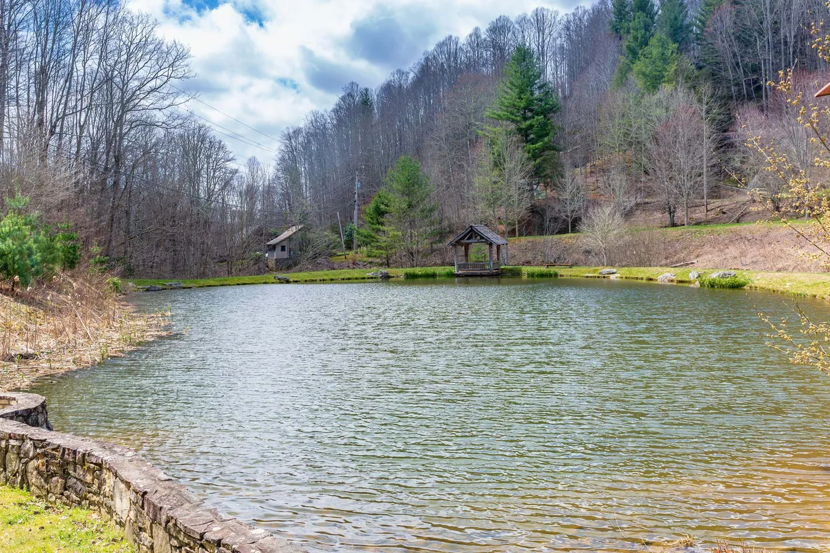 A tranquil pond, charming gazebo, and distant cabin are nestled among mature trees, creating a peaceful setting for fishing, picnicking, and nature walks. The expansive area evokes a sense of relaxation and community connection with the outdoors.