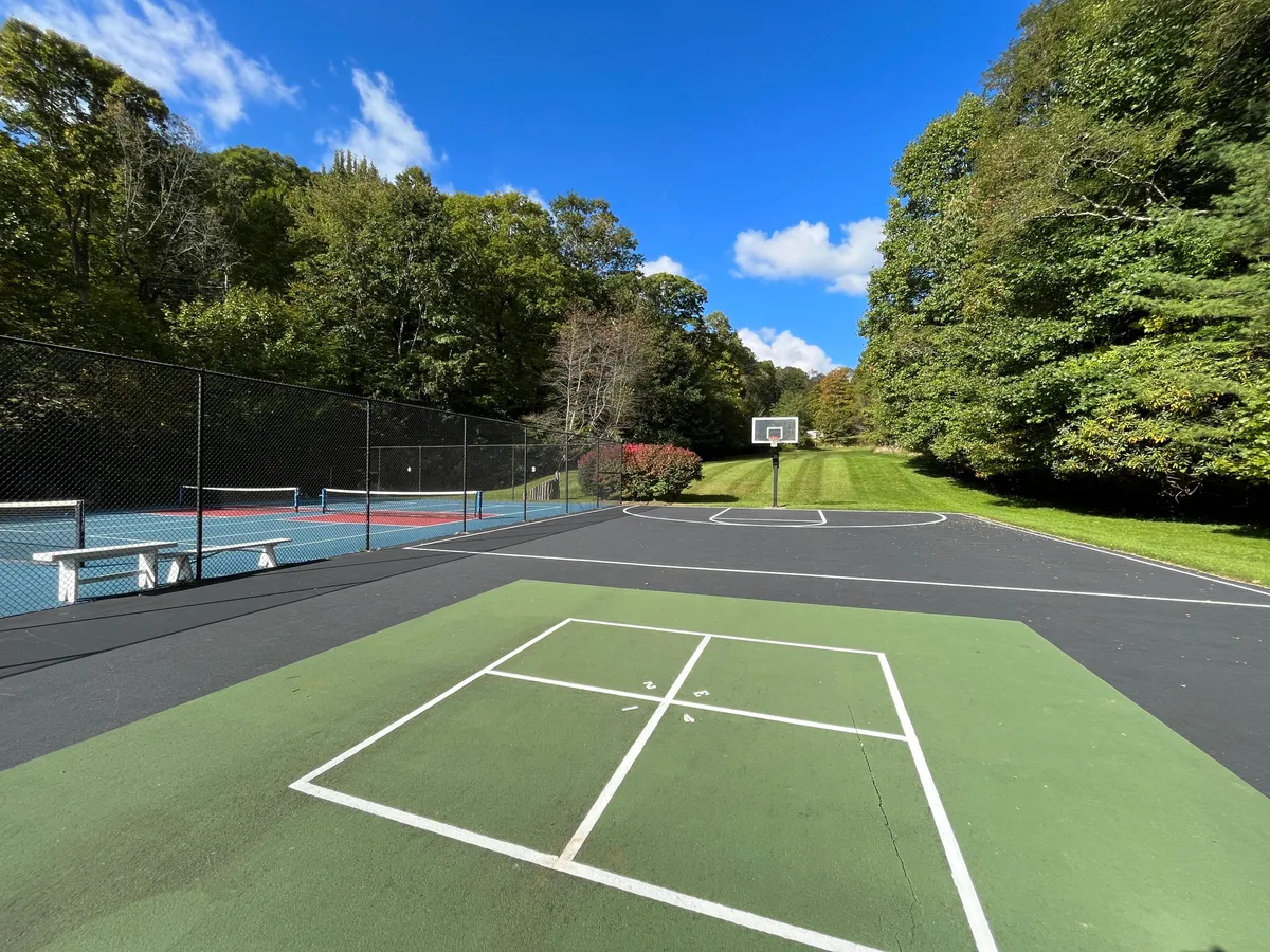 This lively exterior scene features bright green grass, a basketball hoop, and tennis courts surrounded by open space. The area invites families and friends to engage in active outdoor games and sports, highlighting amenities that foster a community-centered lifestyle.
