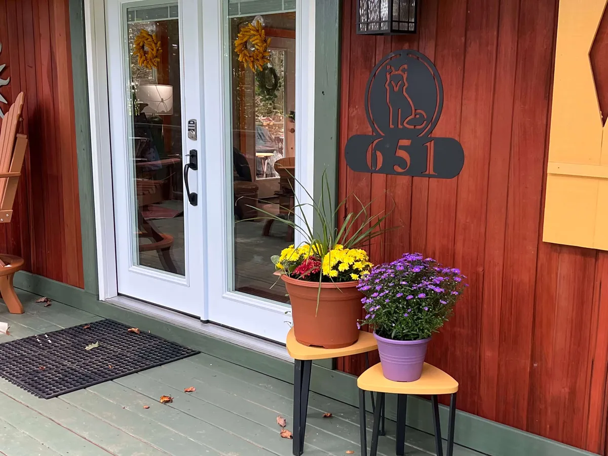 An inviting entrance with double doors, vibrant potted flowers, a house number sign, and a welcoming chair is showcased. The scene radiates warmth and hospitality, representing the sense of safety and exclusivity upon arrival.